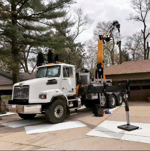 Knuckle boom vehicle showing a difficult tree removal over a roof.