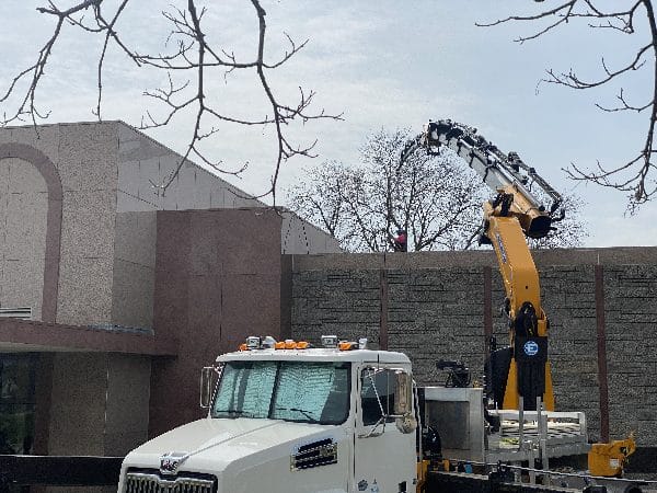 Knuckle boom vehicle showing a difficult tree removal over a roof.