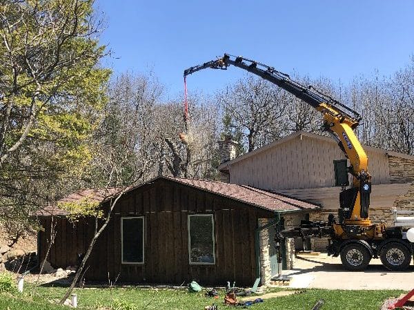 Knuckle boom vehicle showing a difficult tree removal over a roof.