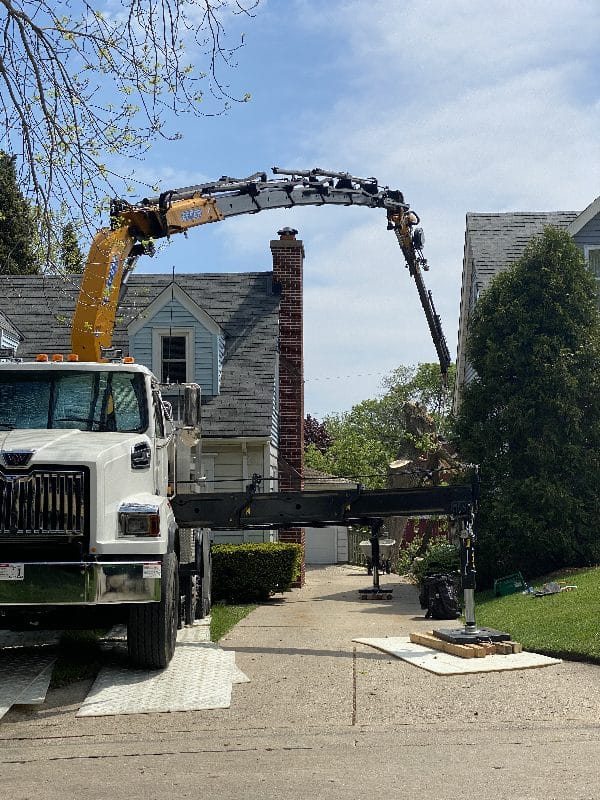 Knuckle boom vehicle showing a difficult tree removal over a roof.